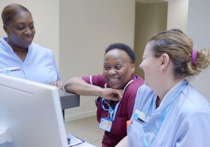 Three nurses laughing and smiling at a computer; ?>