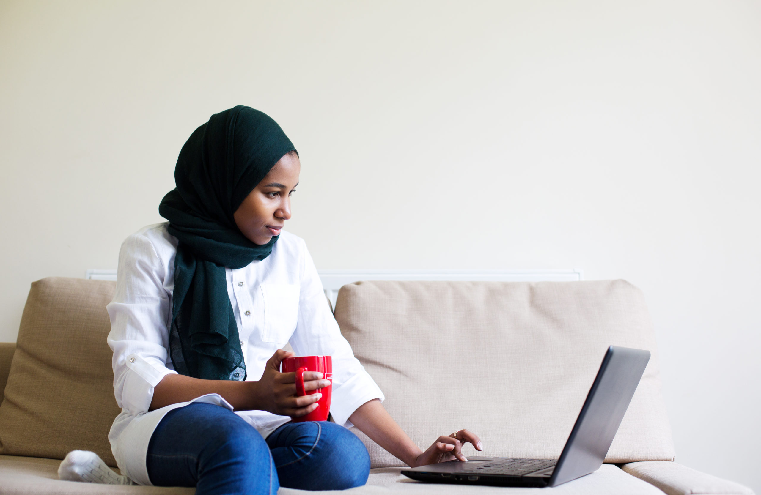 Young muslim woman using laptop while sitting on the sofa