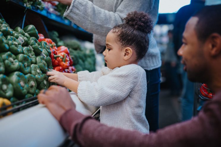 A father helps his young daughter choose vegetables at a supermarket