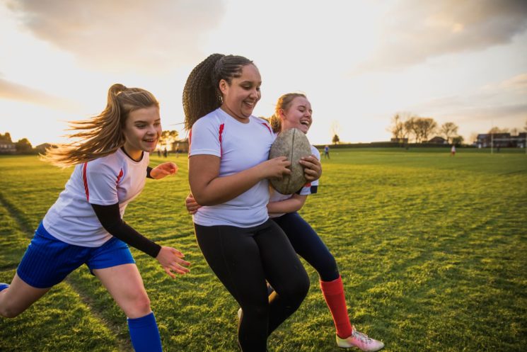 Picture of three girls playing rugby and smiling