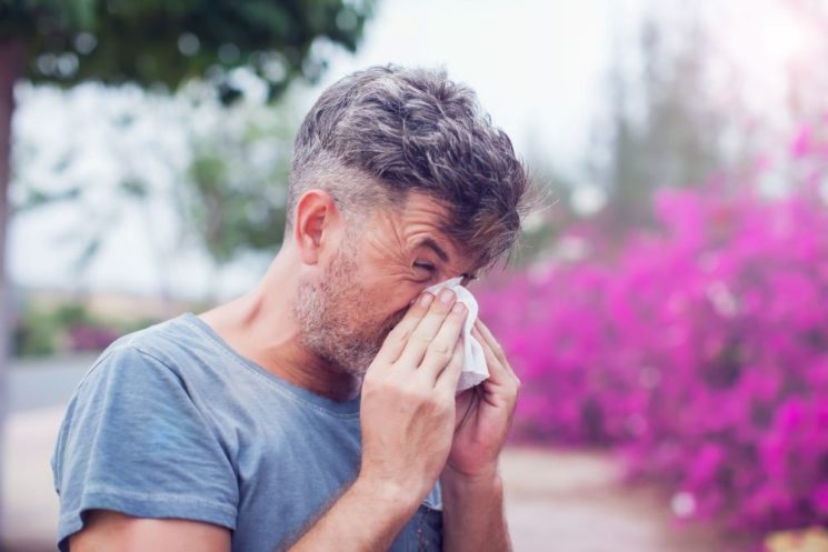 Picture of a man sneezing outdoors due to allergic reaction